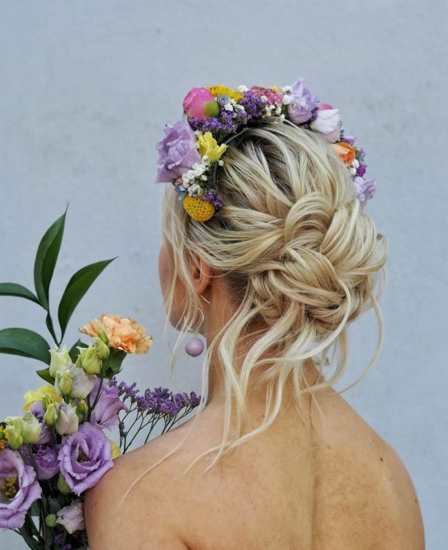Низкая прическа в стиле бохо с повязкой на голову из ярких цветов в тон свадебному букету.